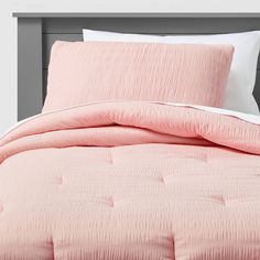 a bed with pink comforter and pillows on top of it, in front of a gray headboard