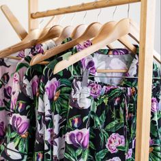 clothes hanging on wooden hangers in front of a white wall with pink and purple flowers