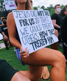 a woman sitting on the ground holding a sign that says jesus didn't die for us so that we could treat others how they treated him