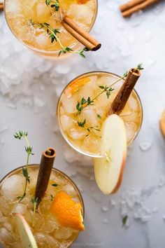 two glasses filled with apple cider and cinnamon stick garnished with fresh herbs