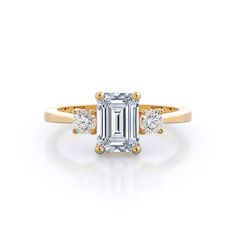 an emerald cut diamond ring with three diamonds on the band and side stones in rose gold