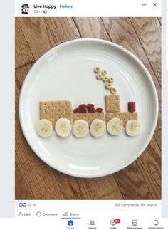 a white plate topped with crackers and bananas on top of a wooden table next to a paper cut out of a train