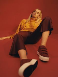 a woman laying on the ground with her legs crossed and wearing brown pants, a yellow sweater and white sneakers