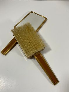 a hair brush sitting on top of a white table next to a gold colored mirror