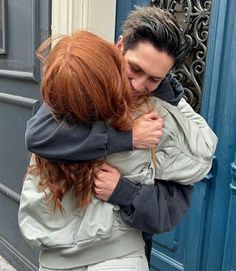 two people hugging each other in front of a blue door