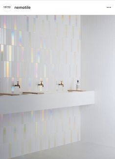 three sinks in a white tiled bathroom with gold faucets and soap dispensers