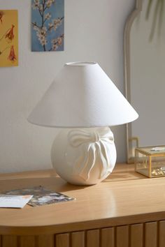 a white lamp sitting on top of a wooden table next to a mirror and framed pictures