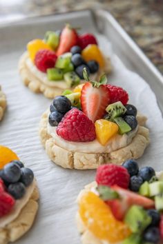 small cookies decorated with fresh fruit are sitting on a baking sheet, ready to be eaten