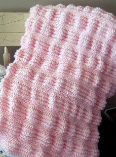 a pink knitted blanket sitting on top of a bed