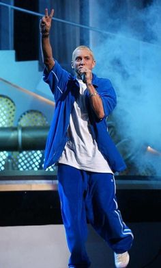 a male in a white shirt and blue pants is on stage with his hand up