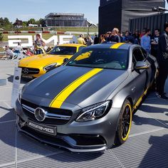 two yellow and gray sports cars parked next to each other on a parking lot with people looking at them