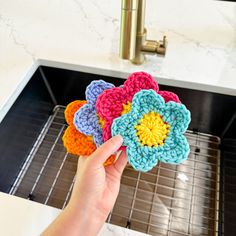a person holding crocheted flowers in front of a sink