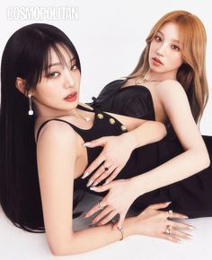 two beautiful young women sitting next to each other on top of a white floor with their arms around each other