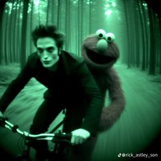 a man riding a bike down a forest filled with trees next to a cookie monster