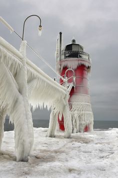 an ice covered lighthouse next to the ocean with icicles on it's legs