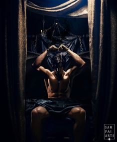a shirtless man sitting in front of a curtain with his hands on his head