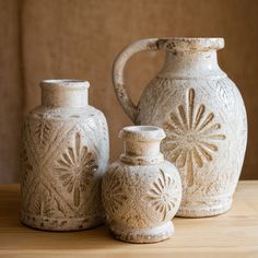 three white vases sitting on top of a wooden table next to an empty bottle