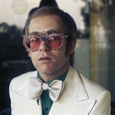 a man in a white suit and bow tie with sunglasses on his face looking at the camera
