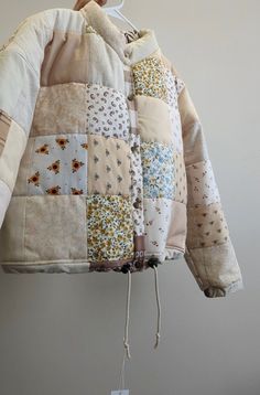 a patchwork jacket hanging up on a hanger next to a wall with a tag