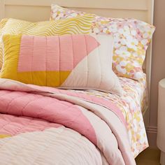 a bed with pink, yellow and white comforter on it's headboard