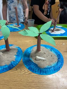 two palm trees made out of paper plates on a table with people in the background