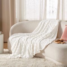 a white couch with a blanket on top of it next to a vase and window