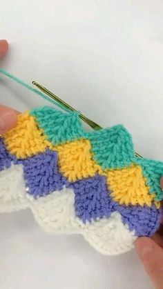 someone crocheting a piece of yarn on top of a white surface with green, yellow and blue stripes