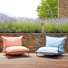 two chairs sitting next to each other on top of a wooden deck with flowers in the background