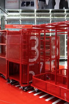 three red carts with numbers on them in a warehouse or retail area, one is empty and the other has two people walking by
