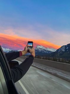 a person taking a photo with their cell phone while driving down the highway at sunset