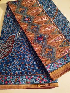 two pieces of blue, red and gold patterned fabric on a table top with a white surface