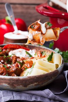 a spoon full of pasta with meat and cheese on it is being lifted from a bowl