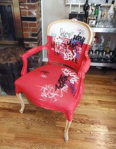 a red chair with graffiti on it in front of a fireplace