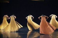 four women in long dresses are standing on a stage with their backs to the camera