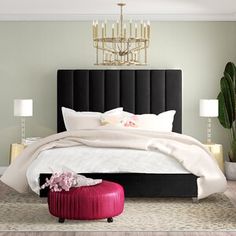 a bedroom with a large bed, chandelier and pink foot stool in front of it