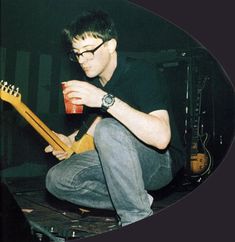 a man sitting on top of a table with a guitar and cup in his hand