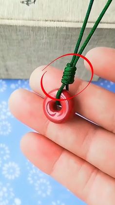 a hand holding a small red object with a green string on it's end