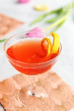 an orange drink in a glass on a doily with tulips behind it