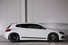 a white car is parked in front of a wall and has black rims on it