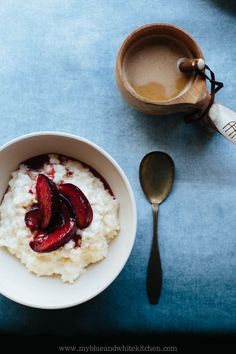 a bowl of oatmeal with sliced plums on top next to a cup of coffee