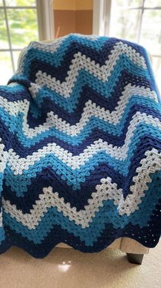 a blue and white crocheted blanket sitting on top of a chair next to a window