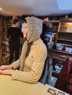 a woman sitting at a table wearing a knitted hat