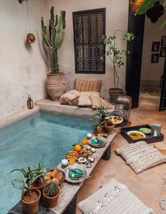an indoor swimming pool with plants and food on the table next to it, surrounded by potted cacti