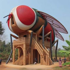 an unusual building made out of bamboo sticks and other materials with people standing around it