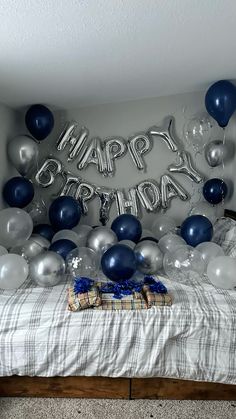 a bed topped with lots of balloons next to a sign that says happy birthday on it
