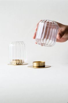 a hand is holding a glass container with gold rims and another object in the background