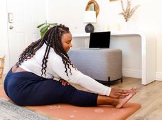 a woman is doing yoga on the floor in front of a laptop computer and coffee table