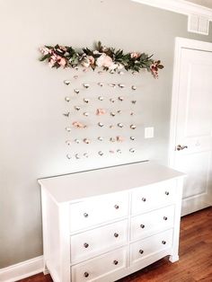 a white dresser with flowers hanging on the wall