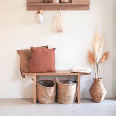 two vases with flowers on the shelf above them and some baskets underneath it in front of a white wall