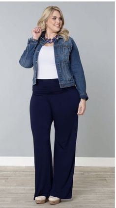 a woman standing in front of a gray wall wearing a denim jacket and wide blue pants